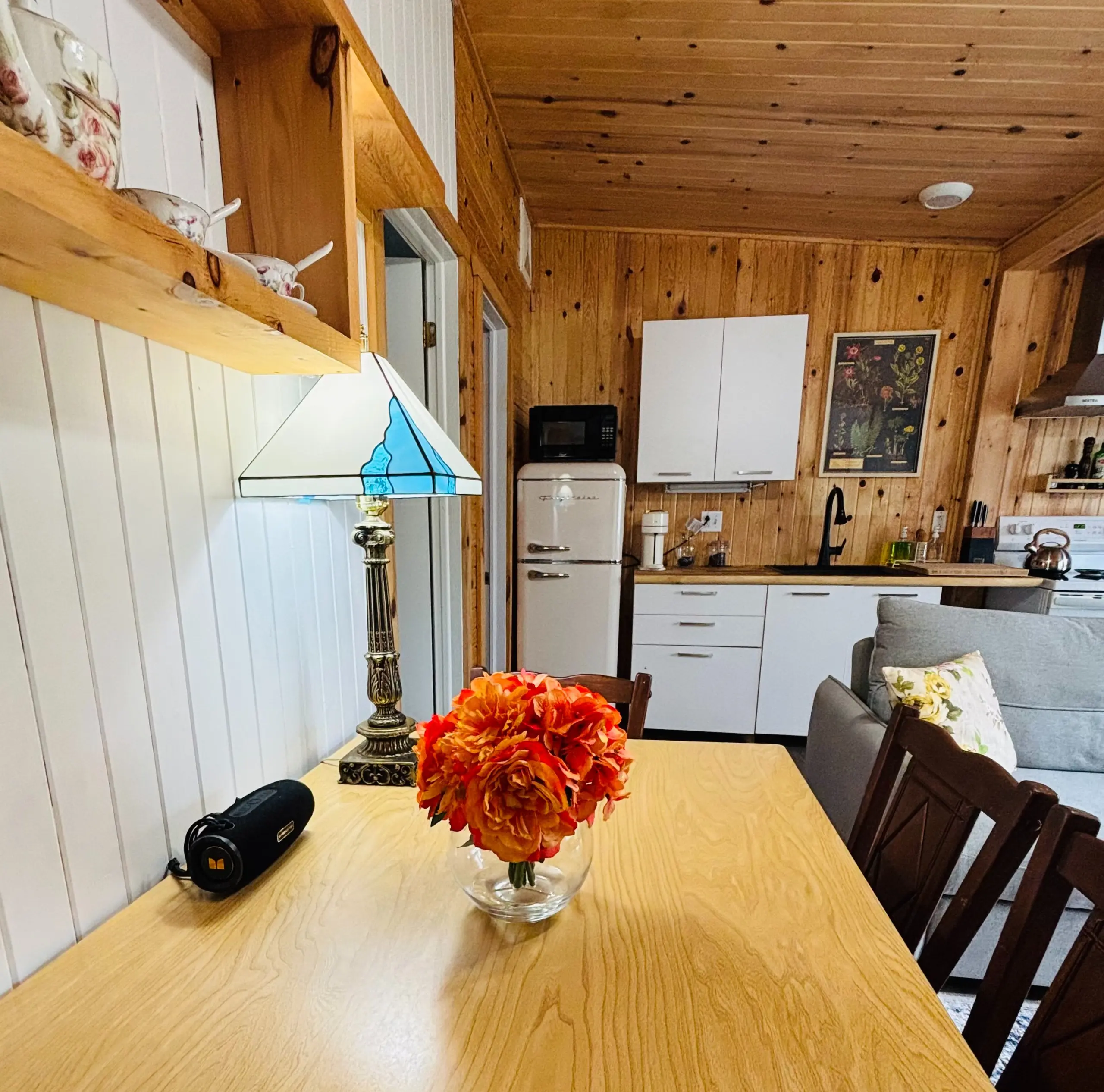 La table de bois blond et son bouquet orangé, la lampe vitrail et, au fond, la cuisine blanche et son réfrigérateur rétro
