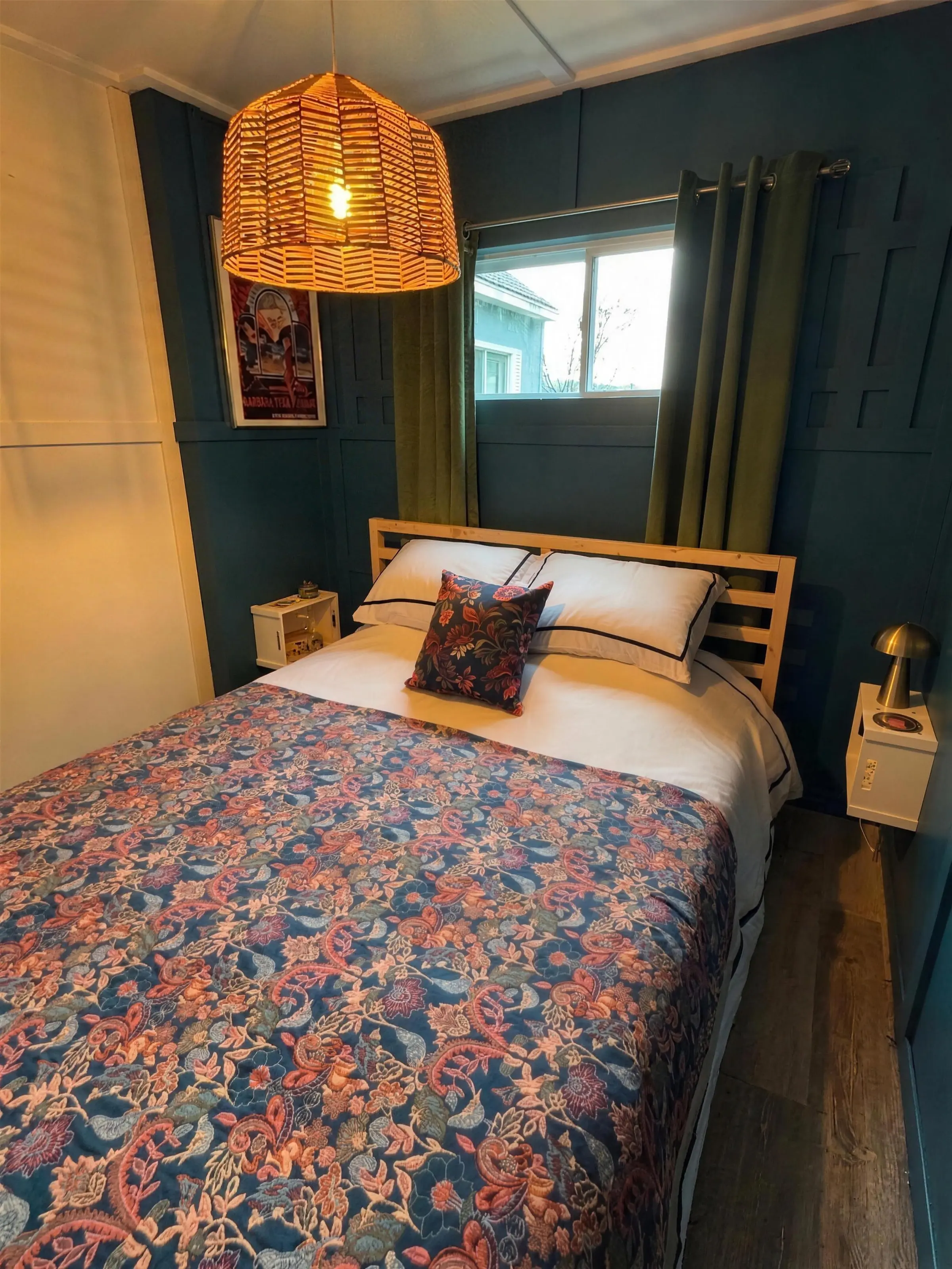 La chambre aux murs bleus : lit queen au couvre-lit fleuri, tête de lit de pin, suspension d’osier et fenêtre aux rideaux verts
