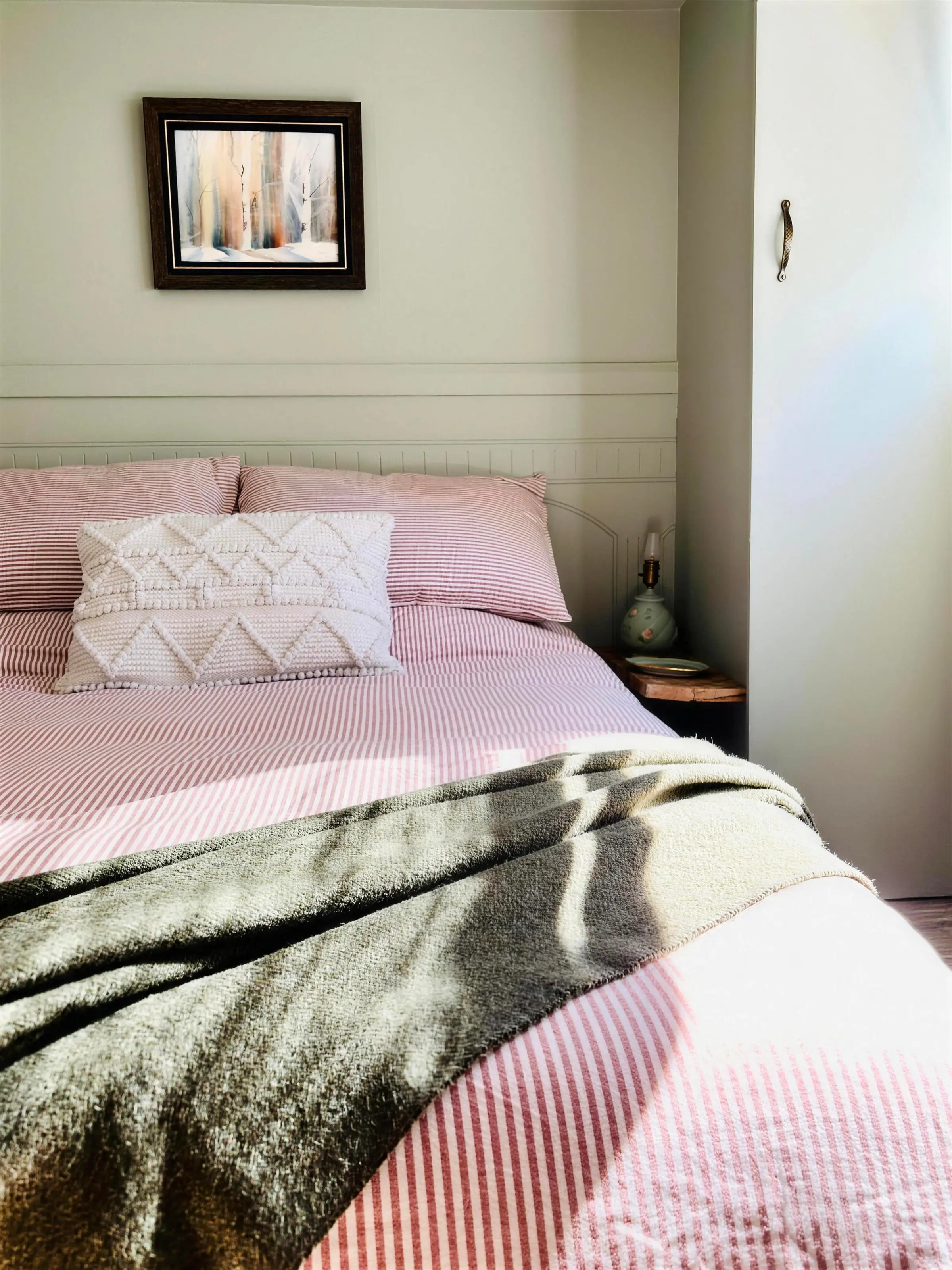 Le lit double du chalet On reste !, ses draps rayés et son jeté de laine olive