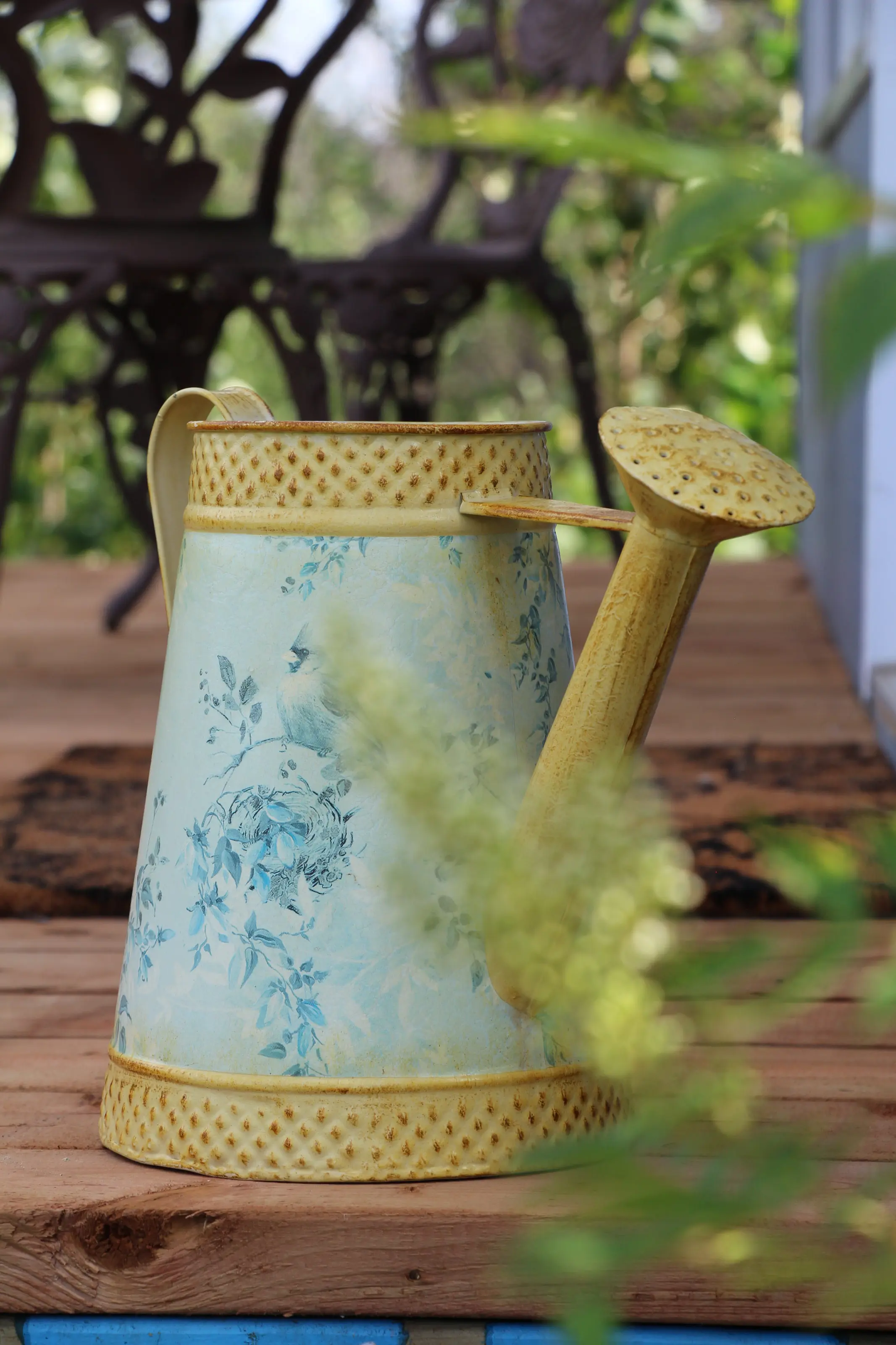 Un arrosoir décoratif posé sur une table de bois, au jardin