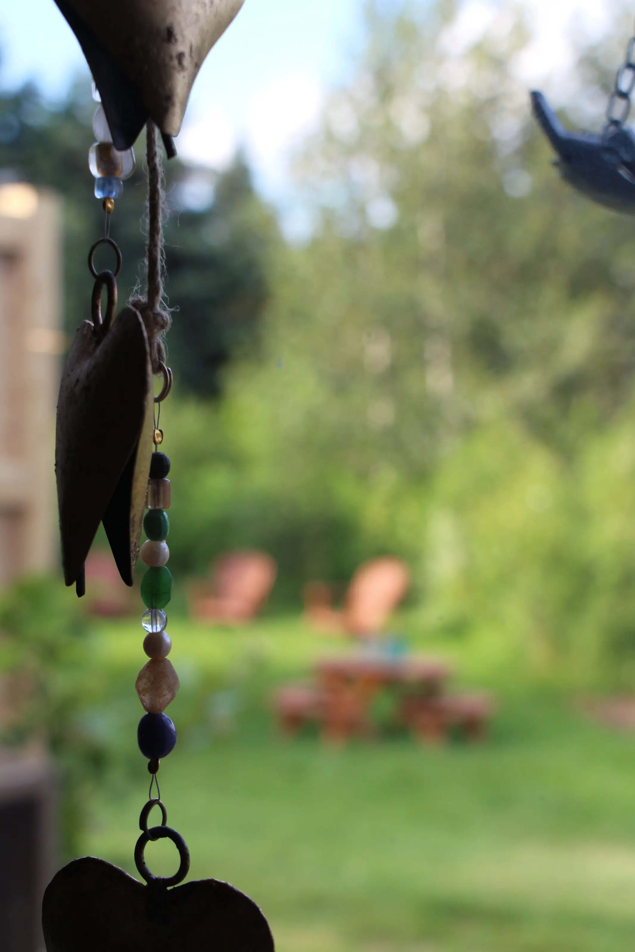 Un carillon de cœurs de métal devant le jardin et ses chaises de bois