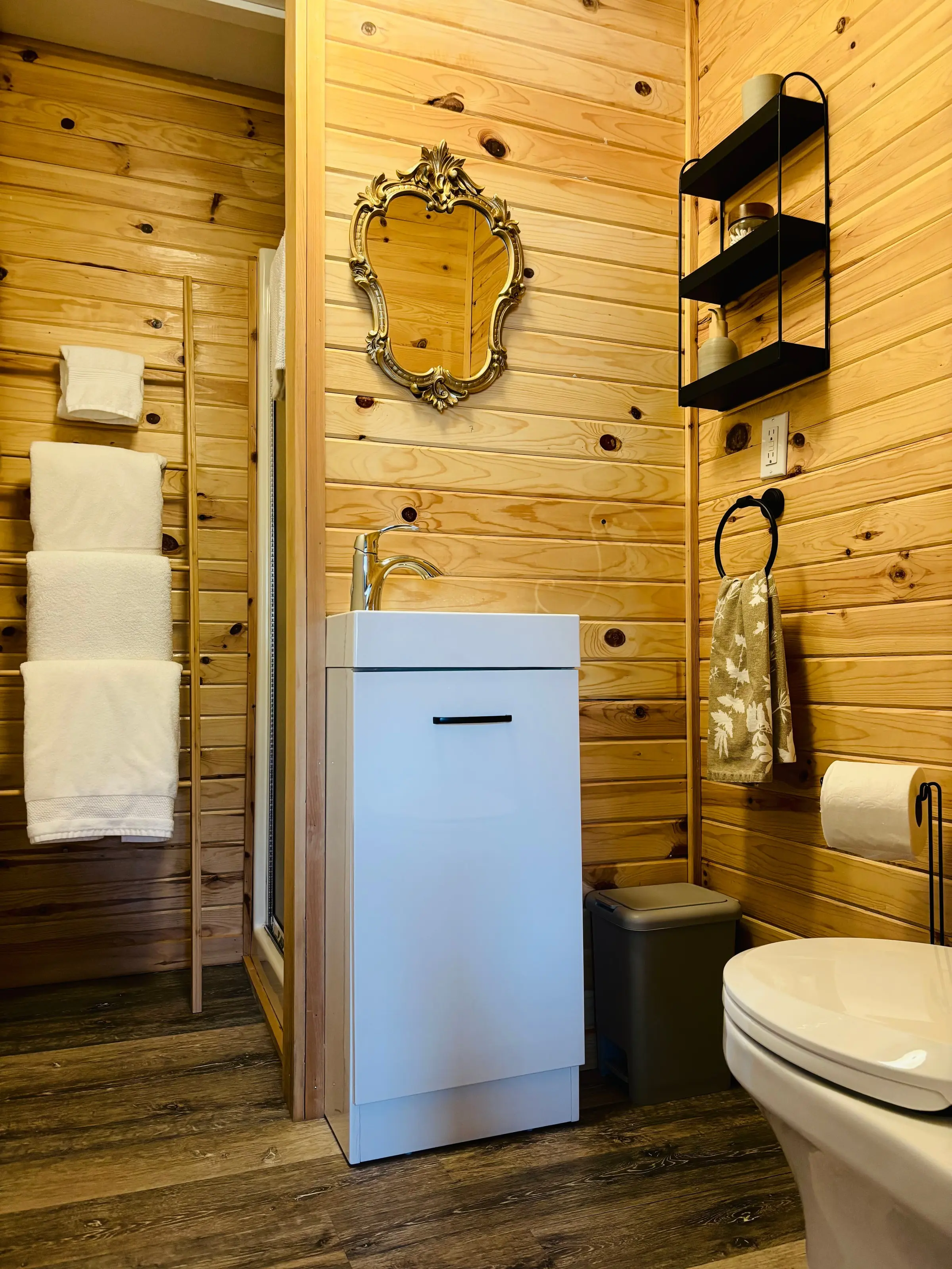 La salle de bain lambrissée de pin, son meuble-lavabo blanc, son miroir doré et son échelle à serviettes