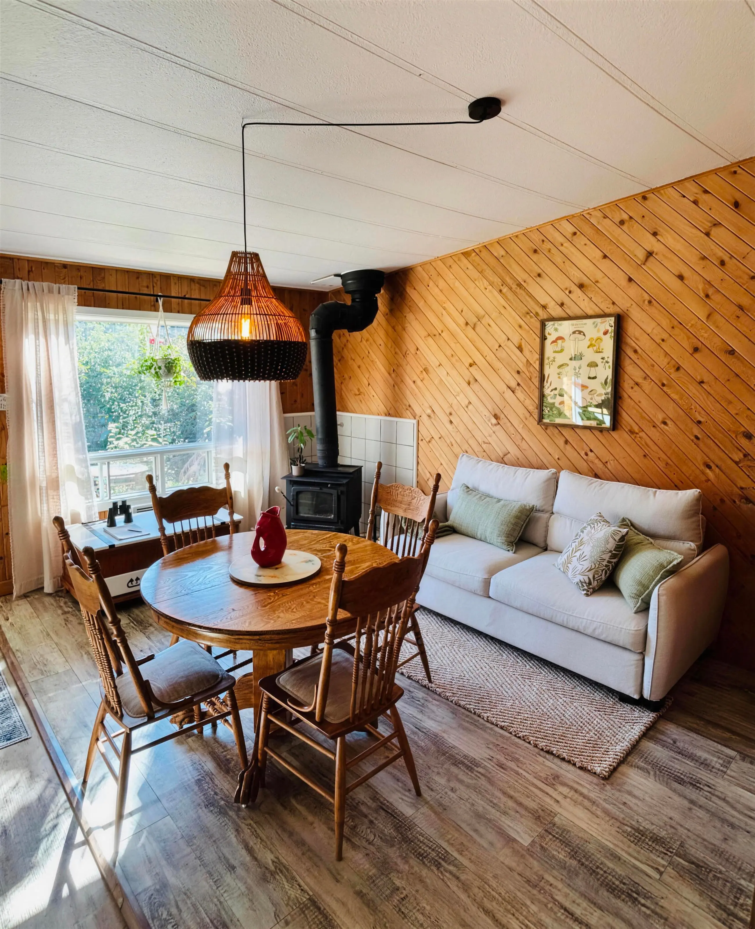 Le salon et le coin repas du chalet On reste !, le canapé blanc et le poêle à bois sous les murs de pin