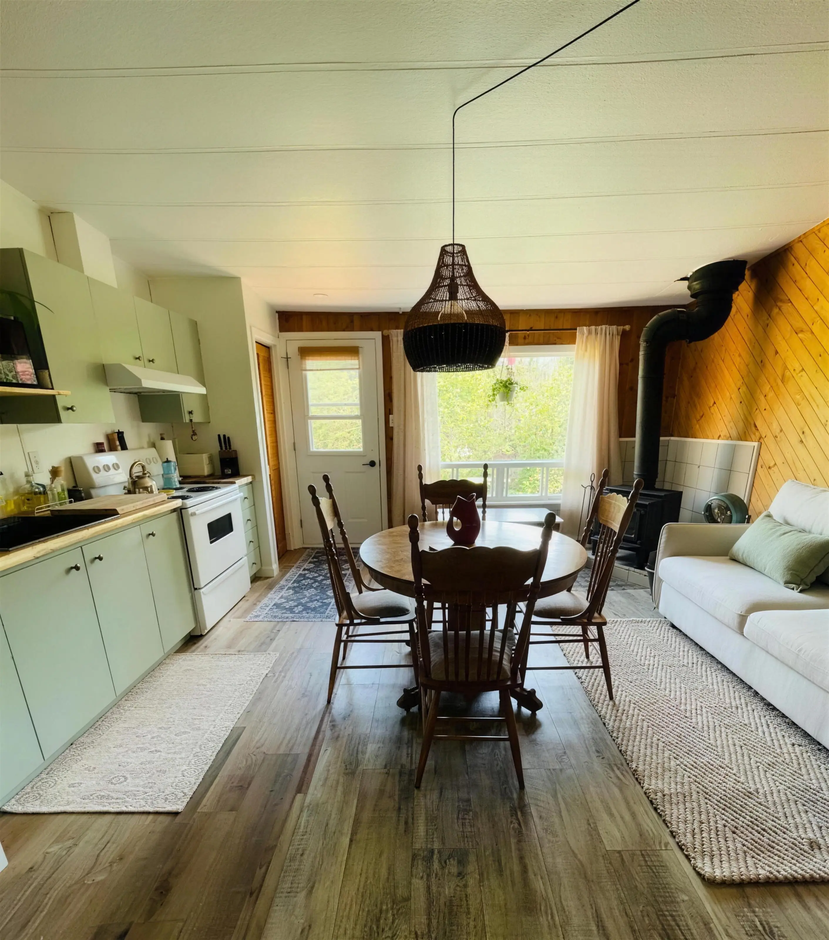 Le salon, le coin repas et la cuisine vert sauge du chalet On reste !, le poêle à bois à droite